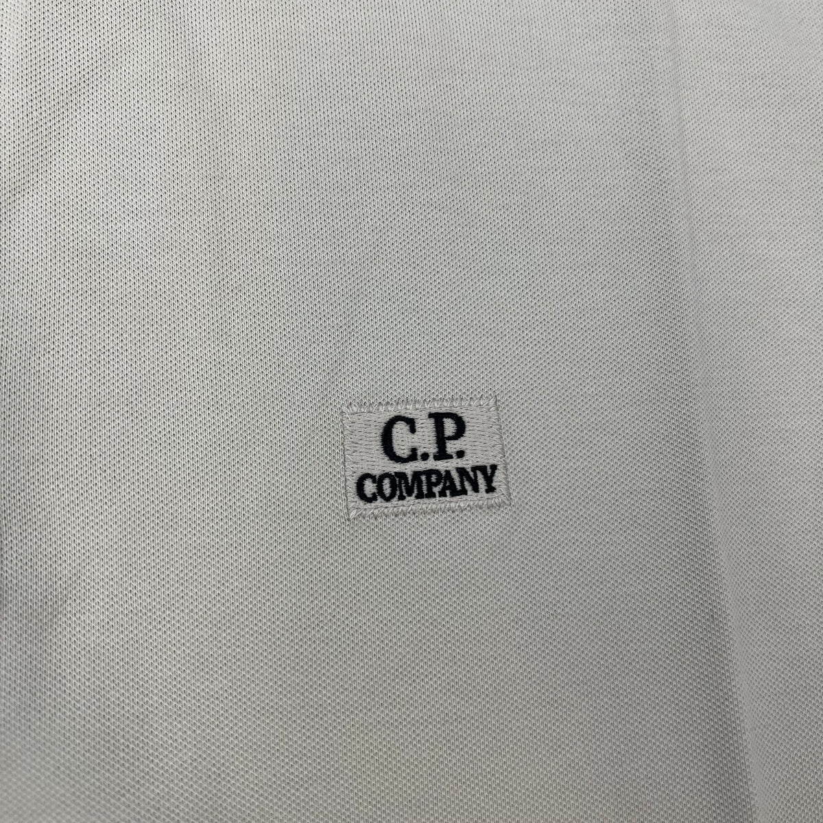Close up view of the embroidered patch logo on a CP Company Long Sleeve Stretch Piquet Polo Shirt in Silver Birch.