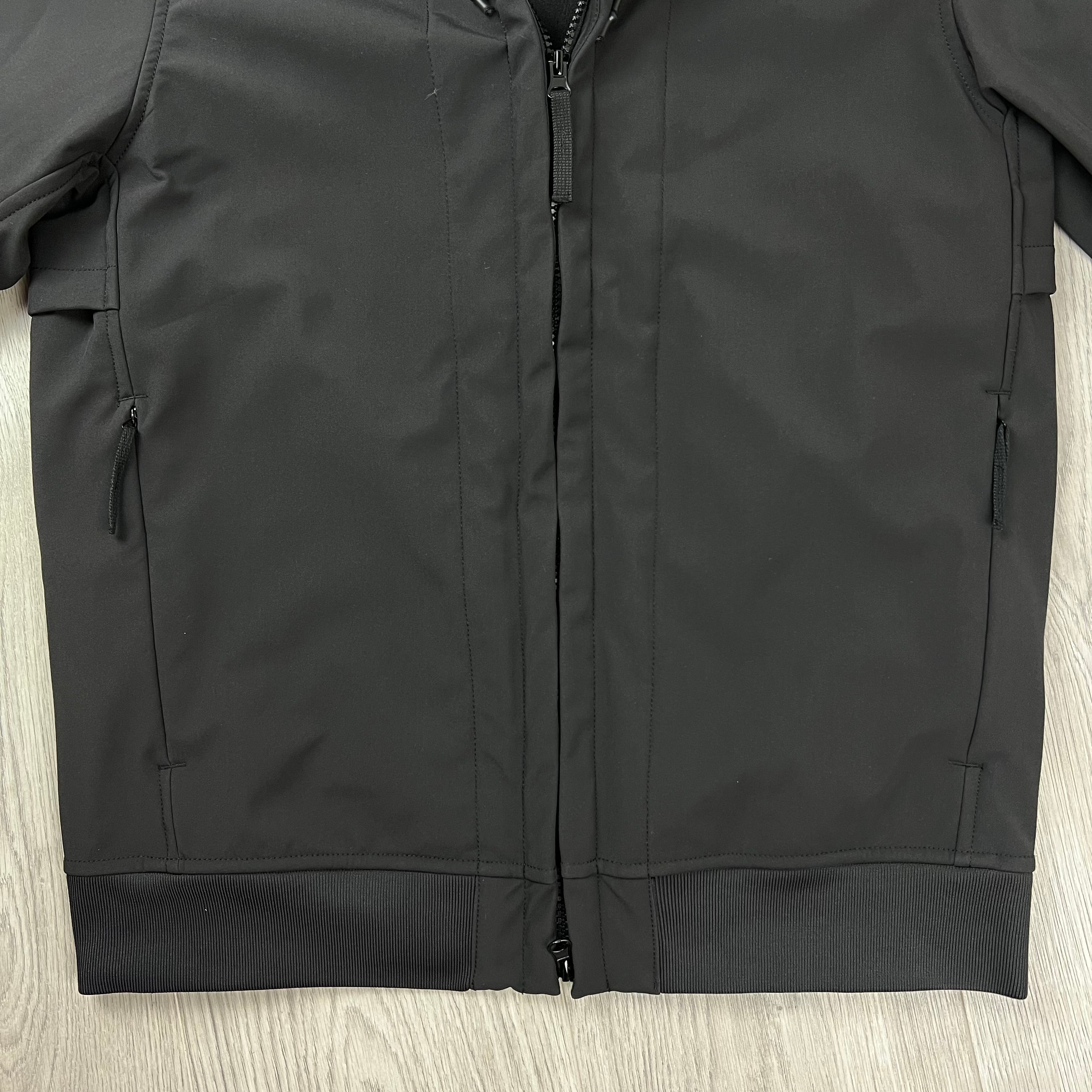 A close up of the Stone Island Soft Shell-Re.dye Jacket in Black showing the front zipper, side zip pockets, and ribbed hem.