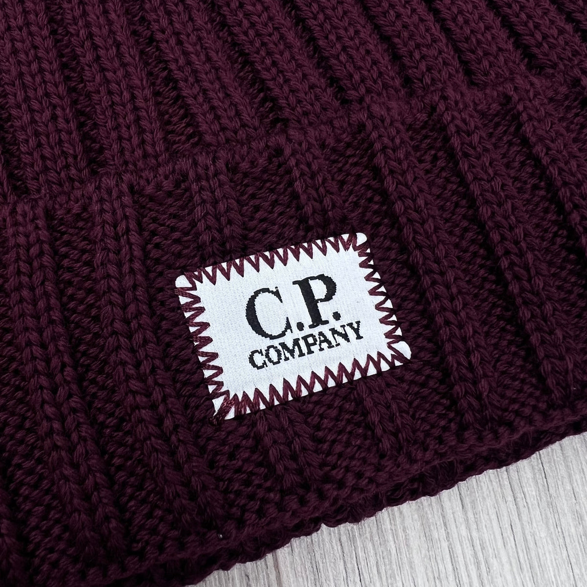 Close up view of the label logo embroidered onto a CP Company Merino Wool Patch Beanie in Andorra.
