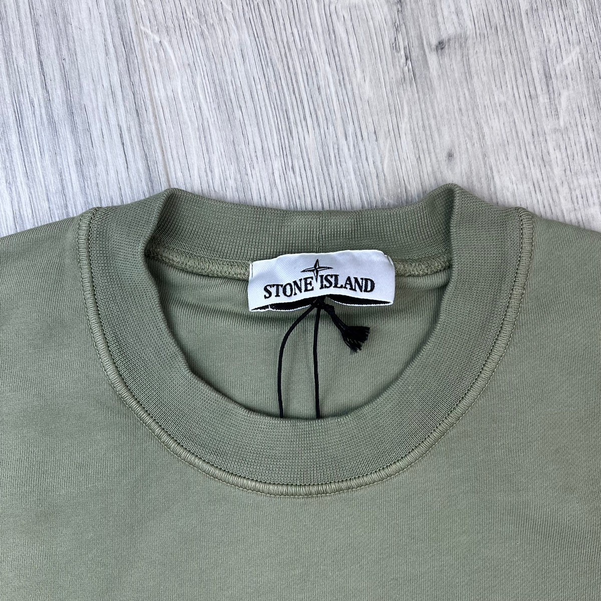 A close up view of the crewneck and label on a Stone Island Crewneck Sweatshirt in Laurel Green.
